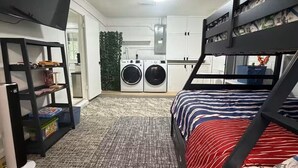 Quarto compacto com beliches, máquina de lavar e estante.