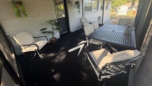 Área de varanda coberta com mesa, cadeiras, plantas em vasos e vista para o exterior.