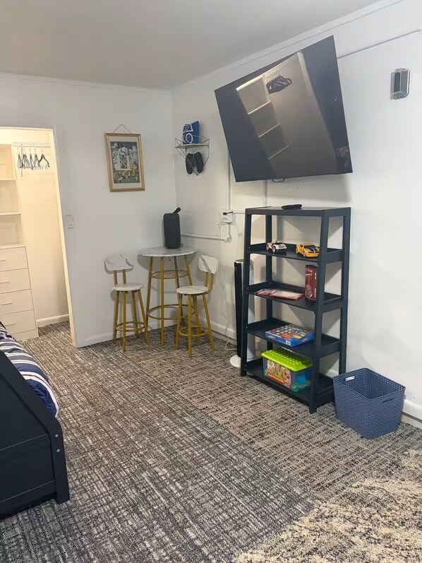 A room with a bed, a TV mounted on the wall, a small table with chairs, a bookshelf, and a carpeted floor. - Rainbow Springs Retreat — Your Perfect Dunnellon Getaway (Dunnellon)