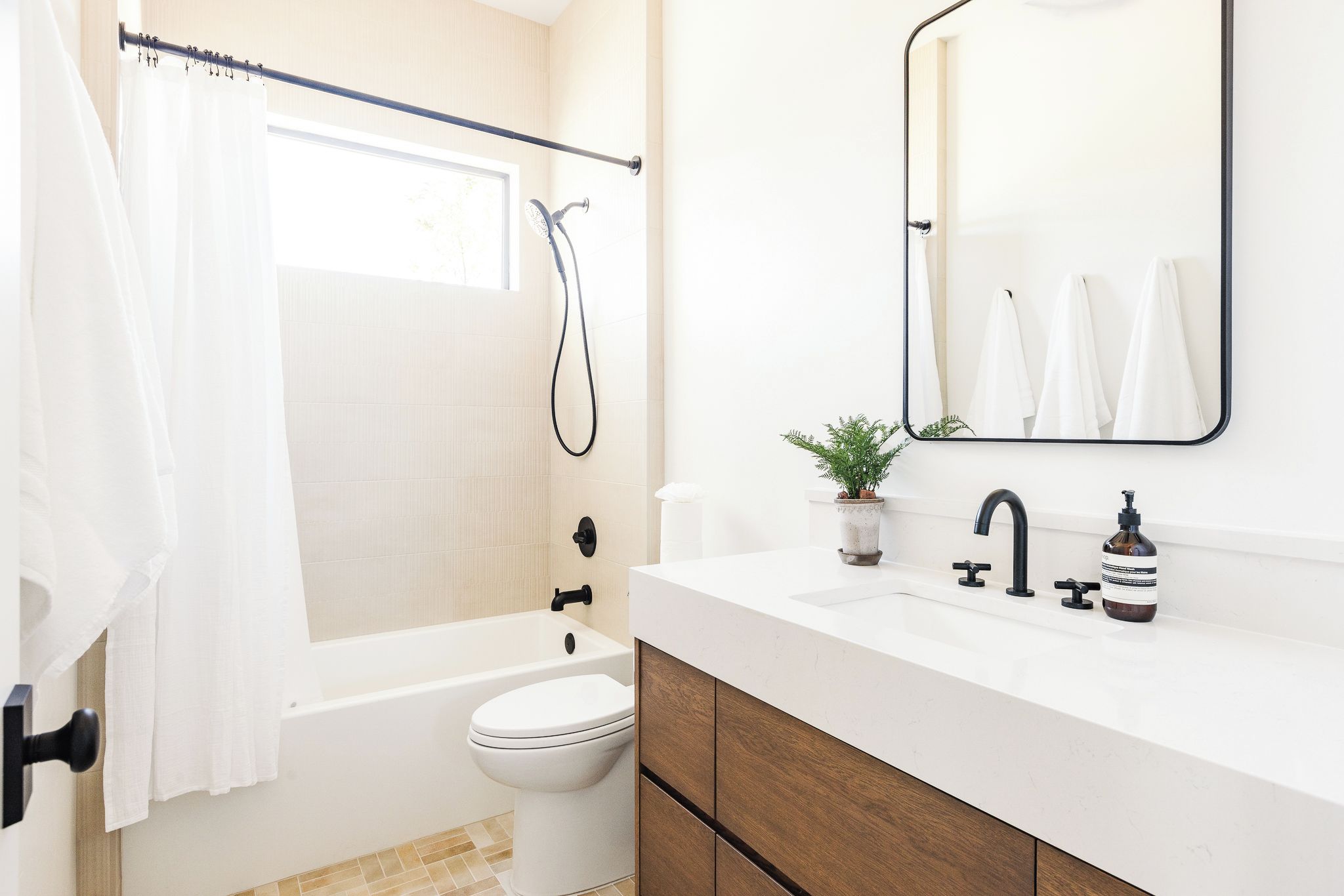 A modern bathroom with a bathtub, toilet, and a sink with a mirror above it.