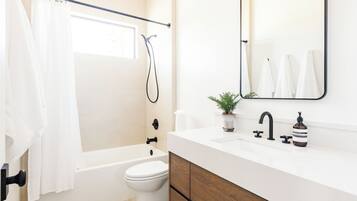 A modern bathroom with a bathtub, toilet, and a sink with a mirror above it.