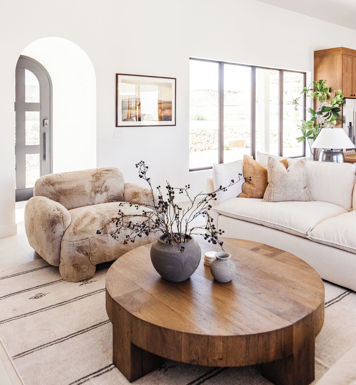 Una sala de estar moderna con una mesa de centro redonda de madera, un sofá color beige y un sillón mullido.