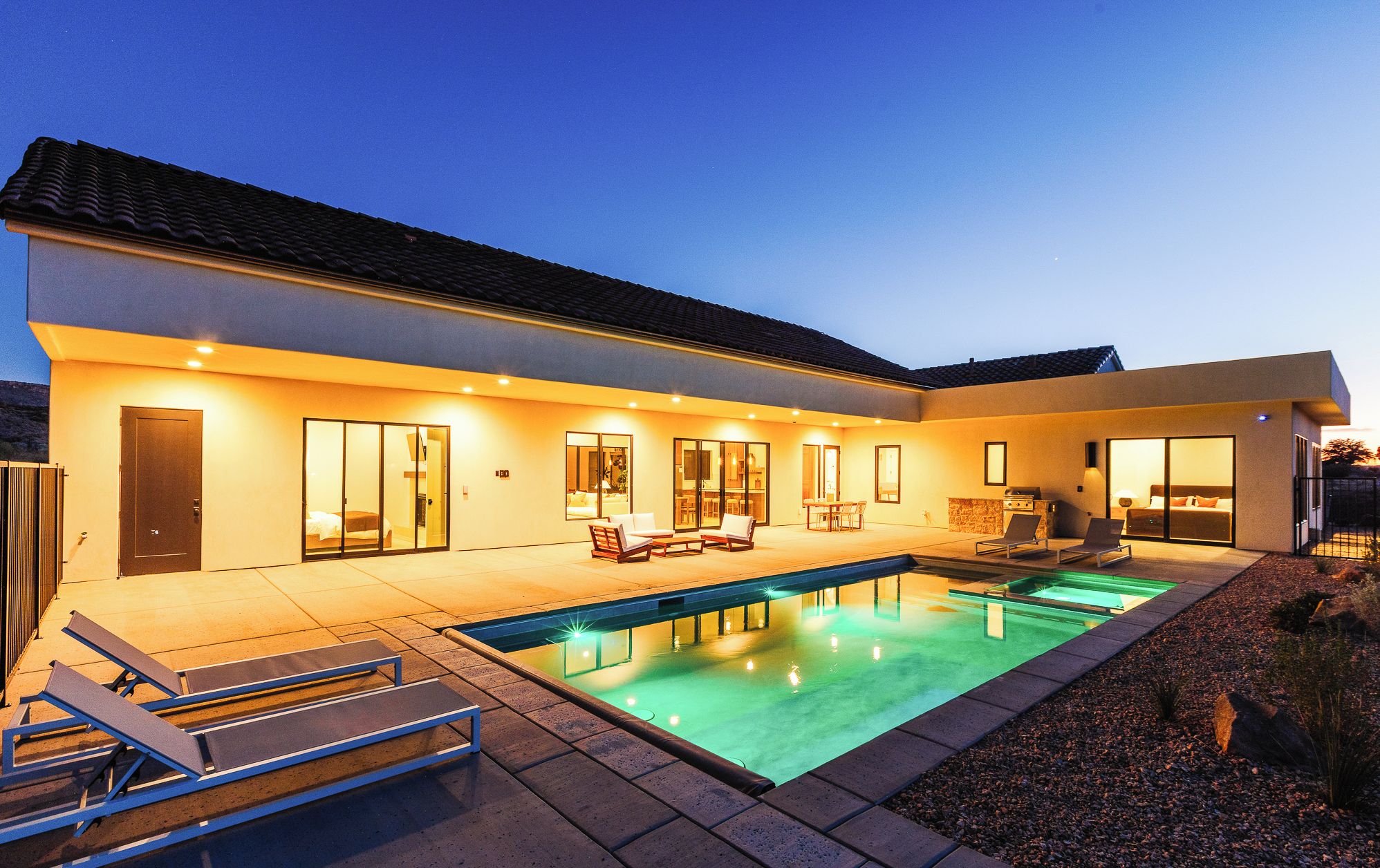 Et moderne hus med swimmingpool, udendørs siddepladser og en oplyst patio.