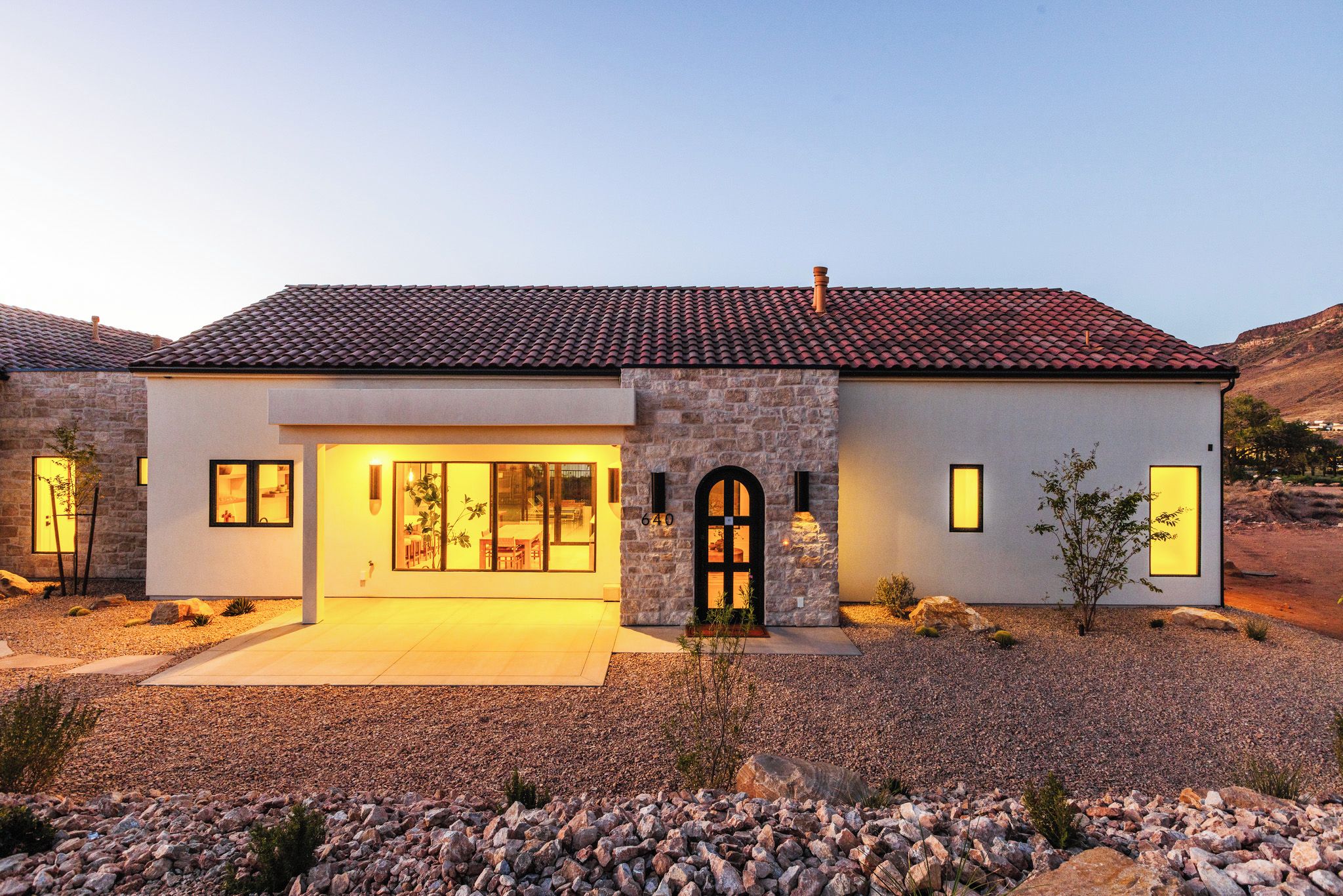 Una casa moderna de dos pisos con fachada de piedra, ventanas amplias y techo de tejas.