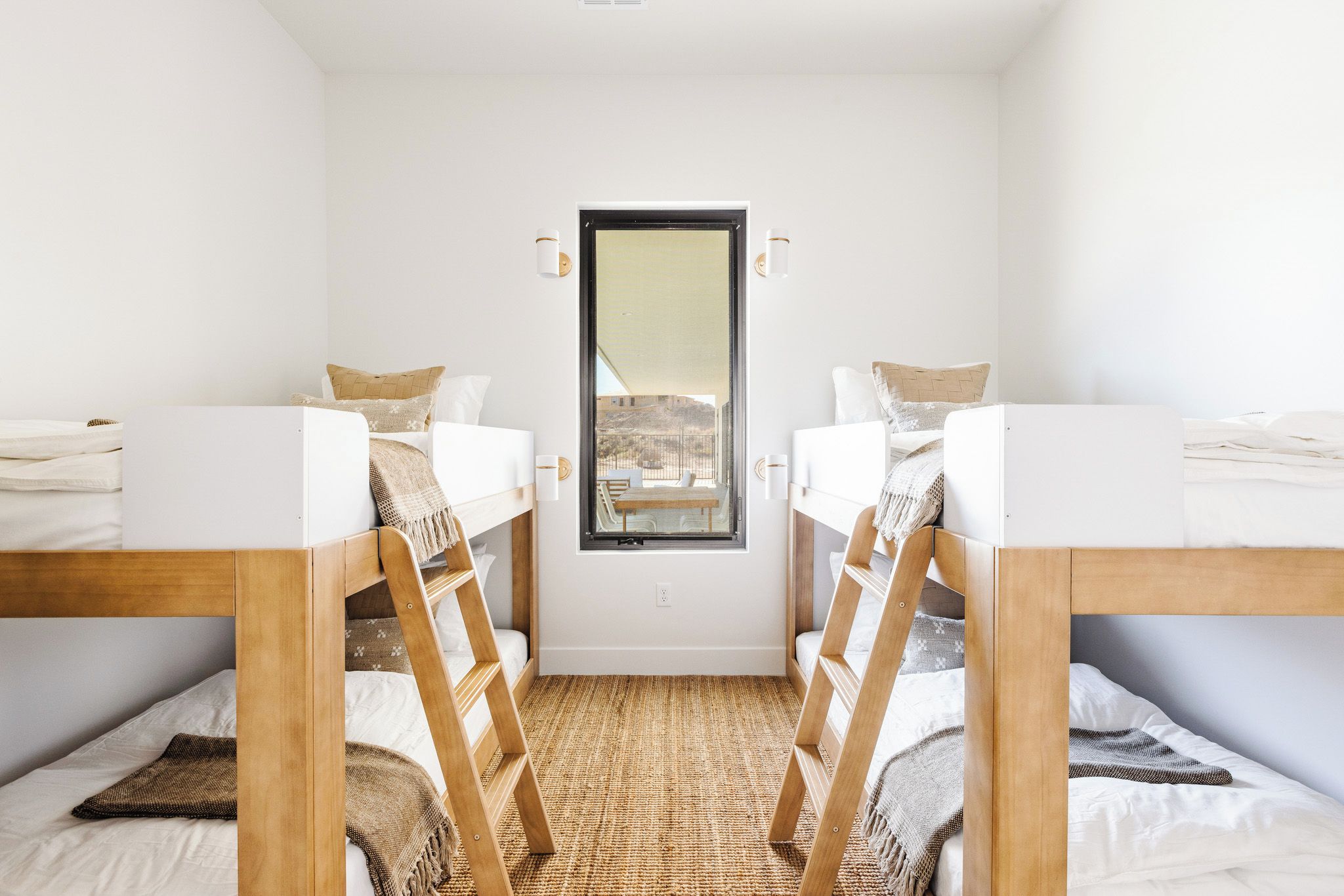 Una habitación con dos literas, una ventana con vistas, y una alfombra tejida en el suelo.