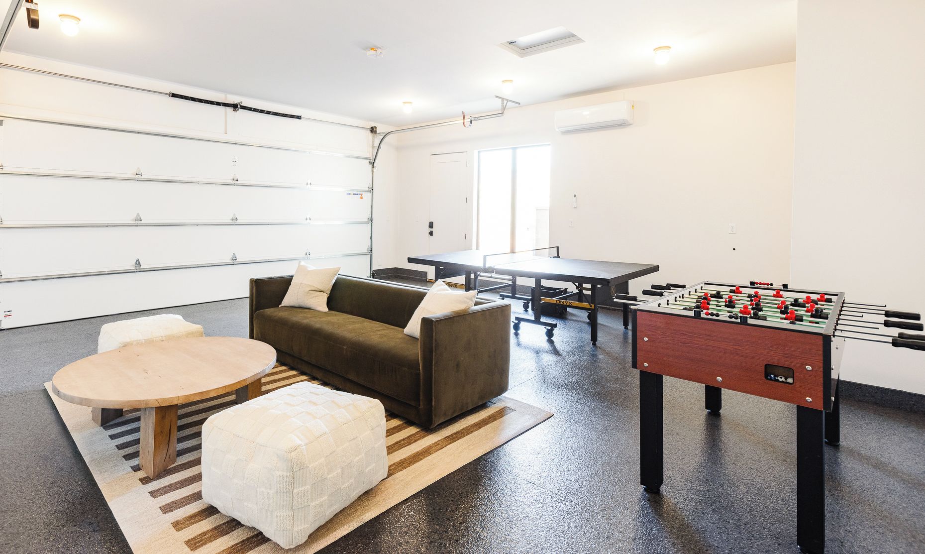 Una habitación con sofá, reposapiés, mesa de futbolín y mesa de ping pong.