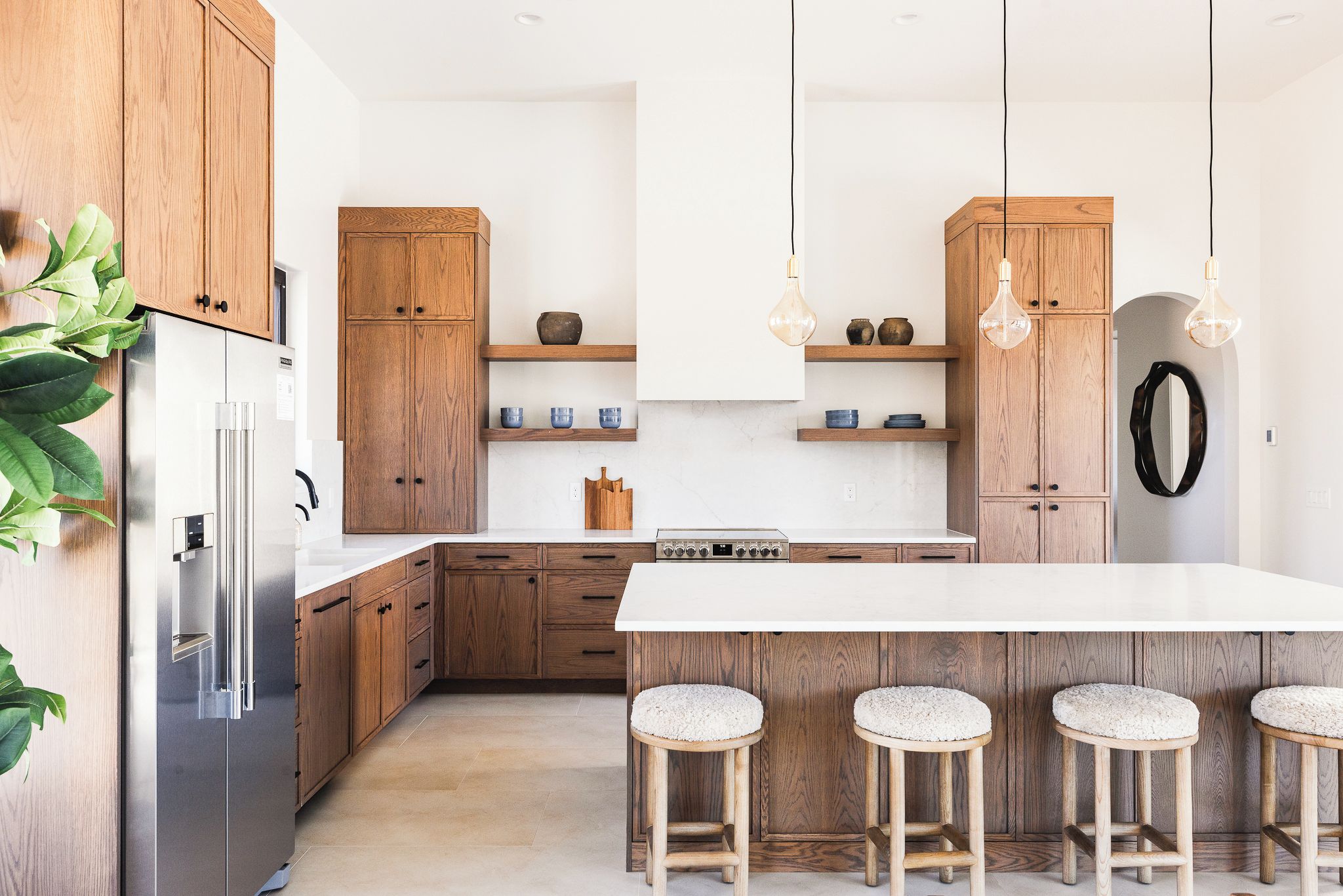 A modern kitchen with wooden cabinets, a stainless steel refrigerator, a central island with stools, and pendant lighting.