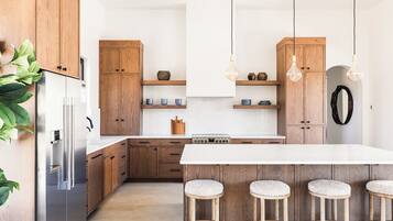 A modern kitchen with wooden cabinets, a stainless steel refrigerator, a central island with stools, and pendant lighting.
