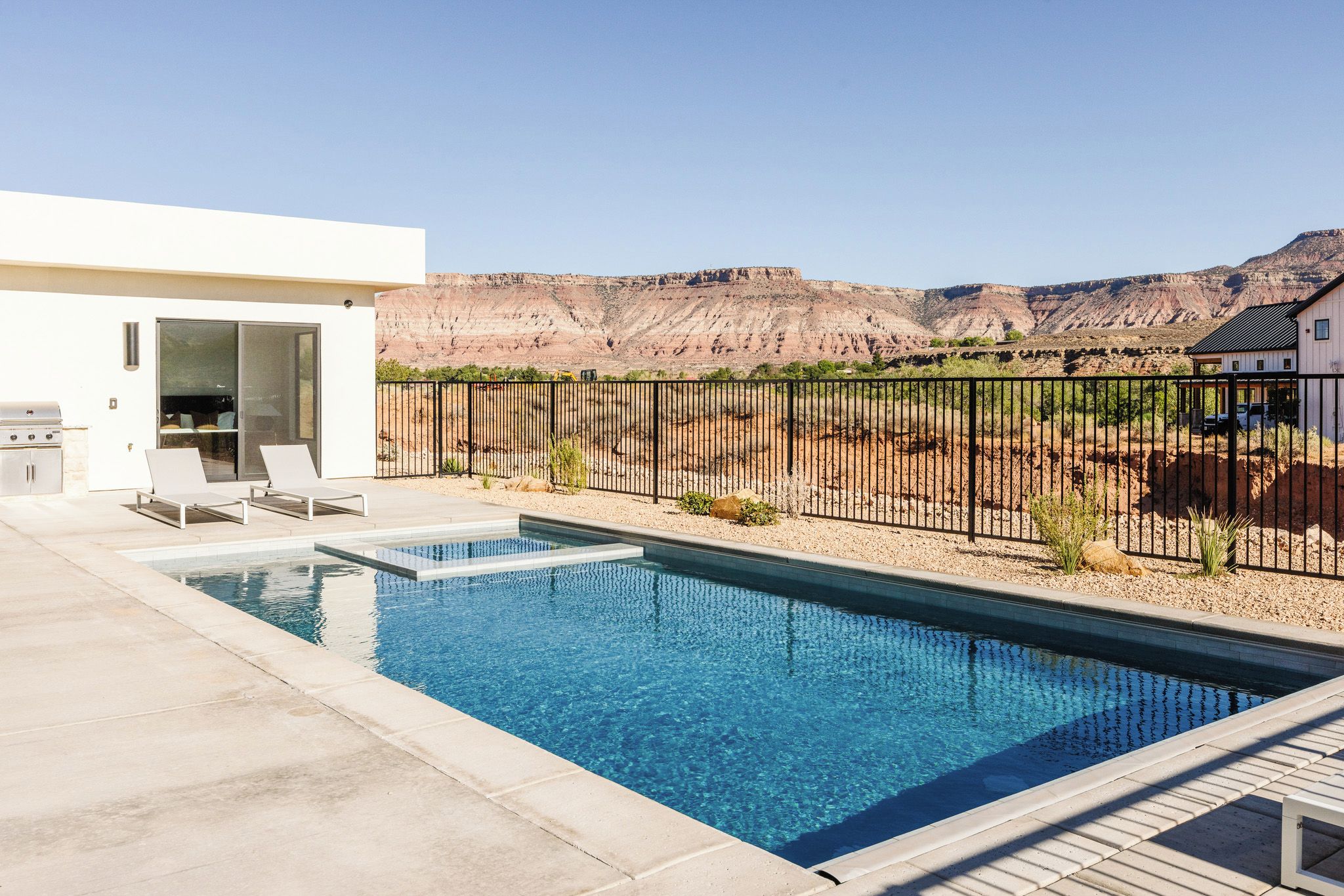 A swimming pool with a patio area, a barbecue grill, and a view of a mountainous landscape.
