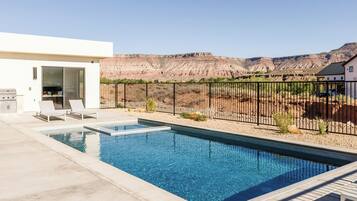 A swimming pool with a patio area, a barbecue grill, and a view of a mountainous landscape.