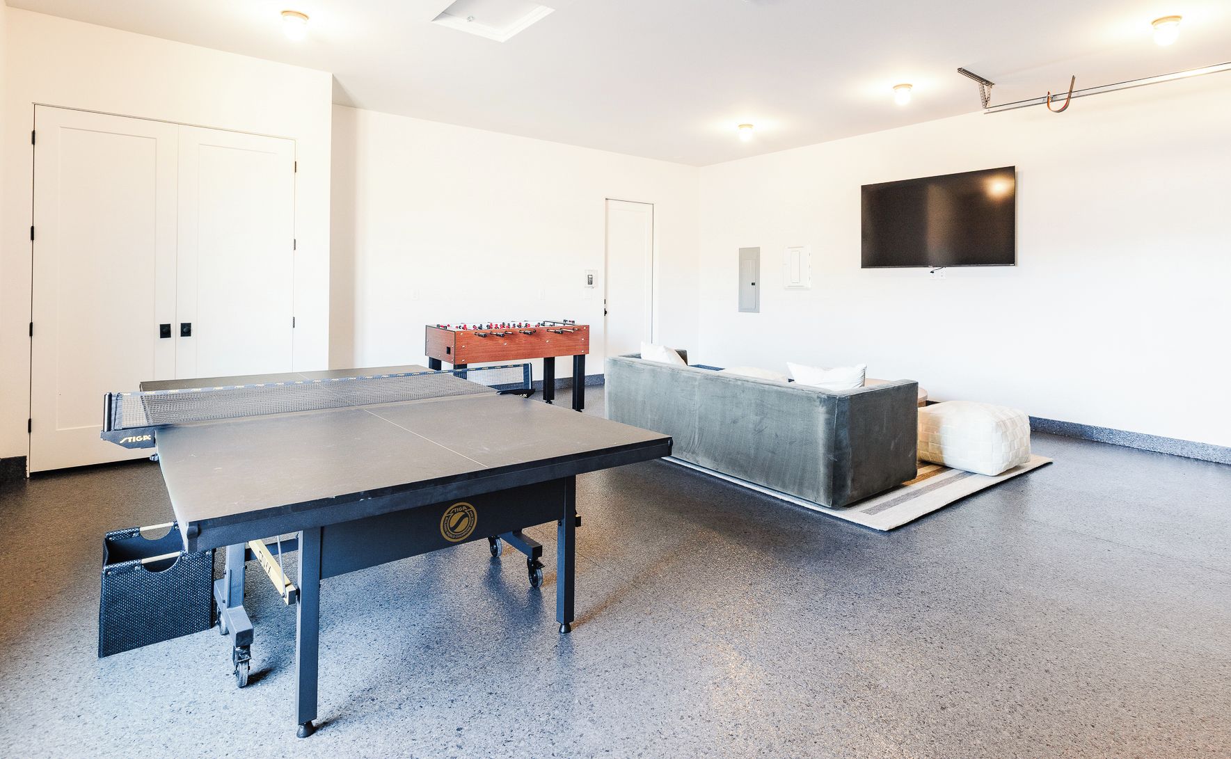 A room with a ping pong table, a sofa, and a foosball table.