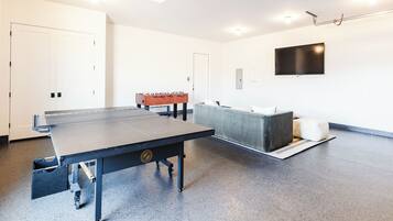 A room with a ping pong table, a sofa, and a foosball table.
