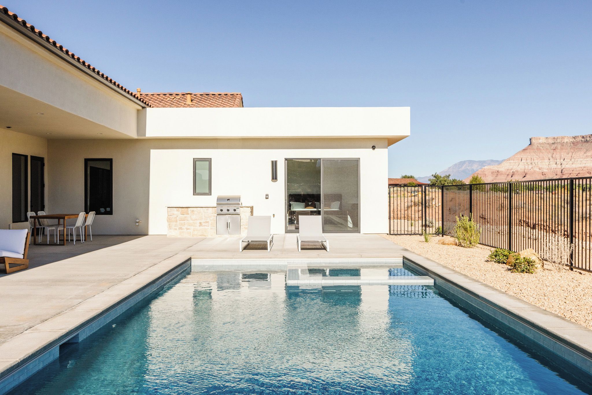 Una casa moderna con piscina, mobiliario de exterior y zona de cocina.