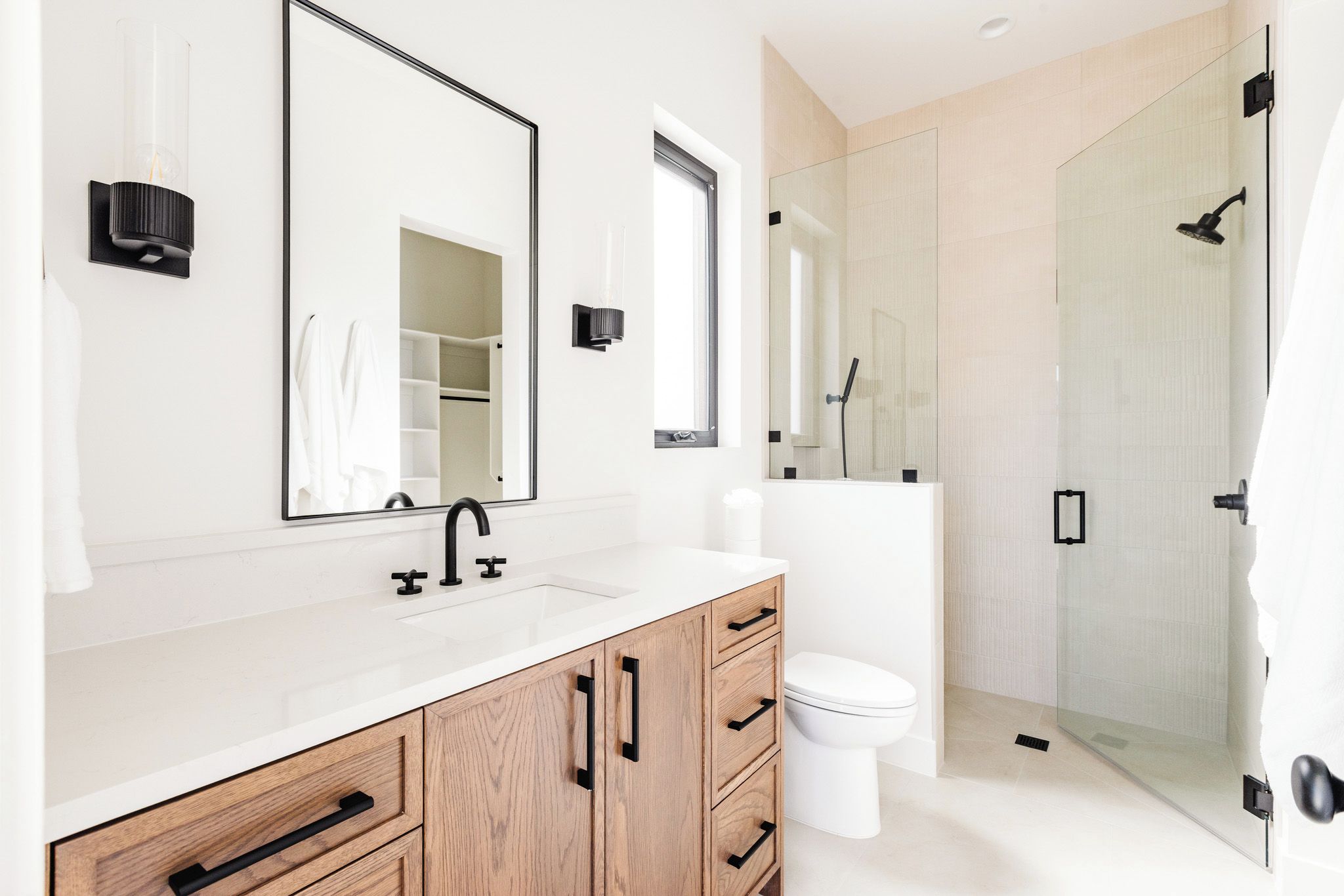 Un baño moderno con tocador blanco, un espejo grande, inodoro y zona de ducha con mampara de cristal.