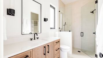 Un baño moderno con tocador blanco, un espejo grande, inodoro y zona de ducha con mampara de cristal.