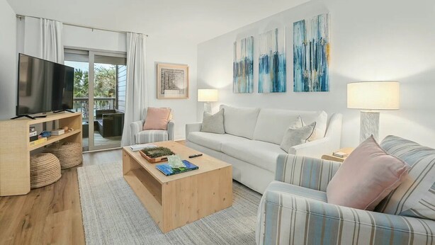 A modern living room with a flat-screen TV, a sofa, a striped armchair, a coffee table, and abstract wall art. - A Place to Remember | Seabrook Convenience (Seabrook Island)