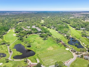 An aerial view of a golf course with multiple water hazards, a well-maintained fairway, and surrounding residential areas. - A Place to Remember | Seabrook Convenience (Seabrook Island)