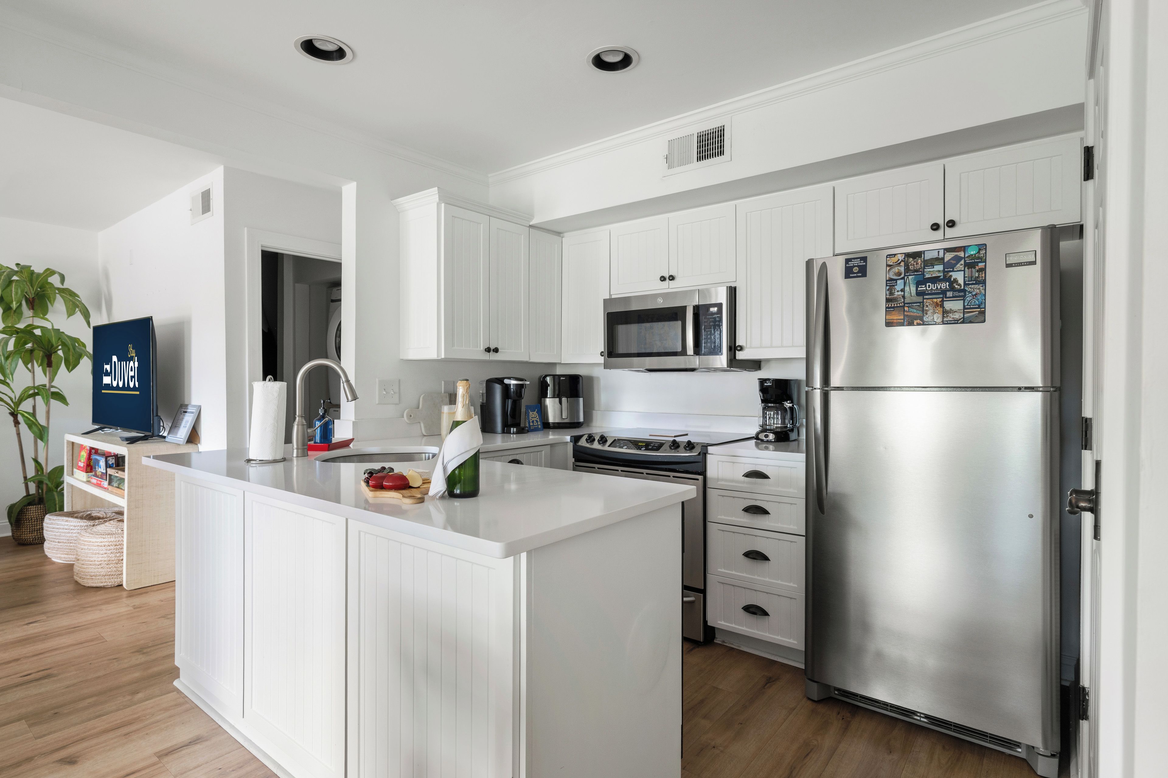 Una cocina moderna con armarios blancos, un refrigerador de acero inoxidable, un microondas y una isla con un lavamanos.