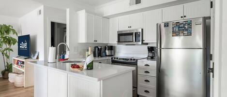 Una cocina moderna con armarios blancos, un refrigerador de acero inoxidable, un microondas y una isla con un lavamanos.