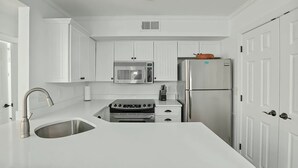 A kitchen with white cabinetry, a stainless steel sink, a built-in oven, a microwave, and a refrigerator. - A Place to Remember | Seabrook Convenience (Seabrook Island)