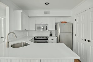 A kitchen with white cabinetry, a stainless steel sink, a built-in oven, a microwave, and a refrigerator. - A Place to Remember | Seabrook Convenience (Seabrook Island)