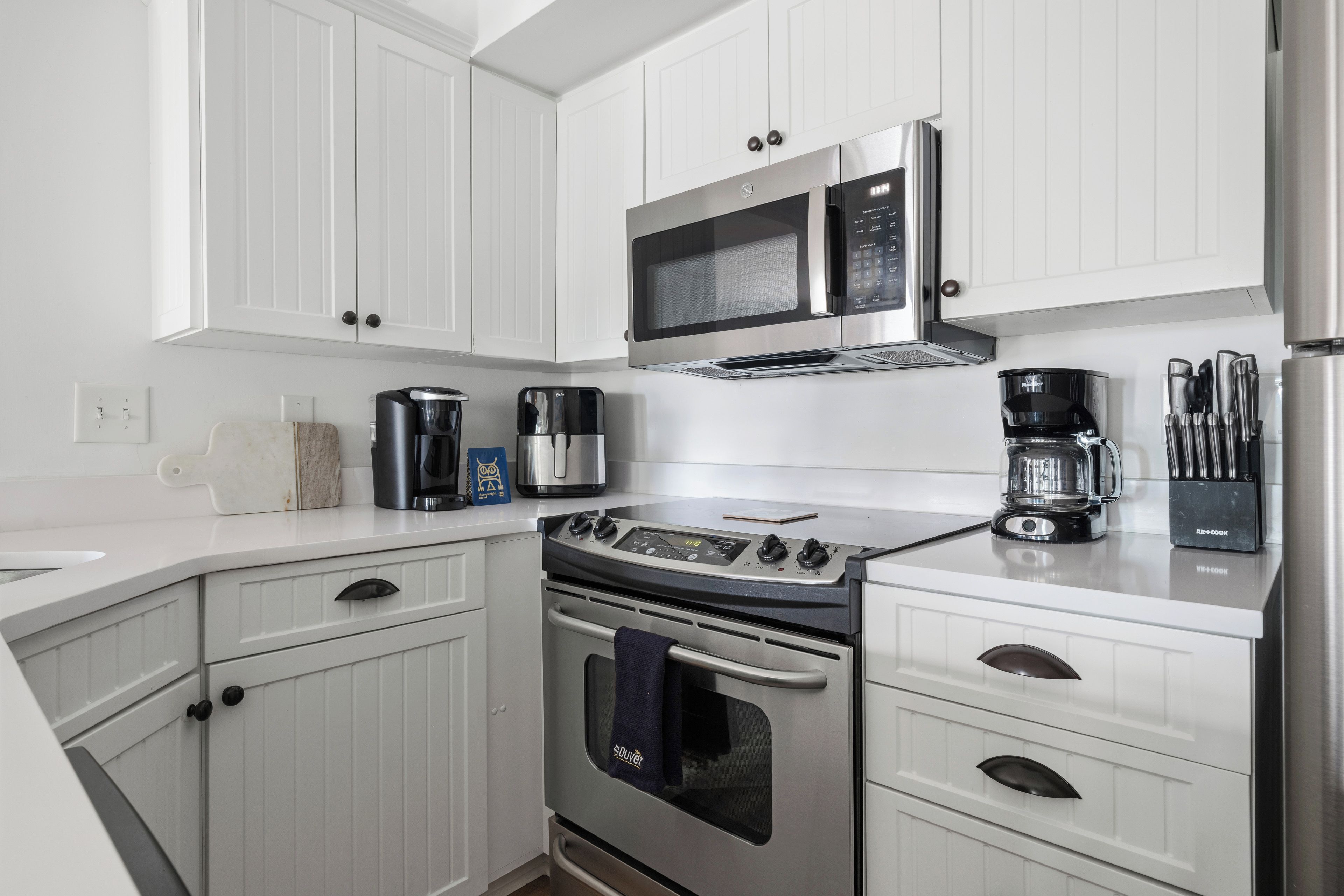 A modern kitchen with white cabinetry, a stainless steel range, a microwave, and a coffee maker.