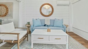 A room with a white sofa, a white coffee table, and a round mirror on the wall. - A Place to Remember | Seabrook Convenience (Seabrook Island)