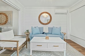 A room with a white sofa, a white coffee table, and a round mirror on the wall. - A Place to Remember | Seabrook Convenience (Seabrook Island)