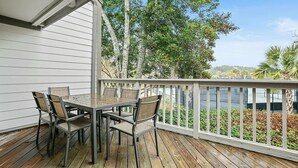 A wooden deck with a table and chairs, overlooking a landscaped area with trees and a fence. - A Place to Remember | Seabrook Convenience (Seabrook Island)