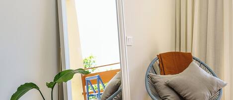 A room with a large mirror, a potted plant, a chair with cushions, and a view through a door.
