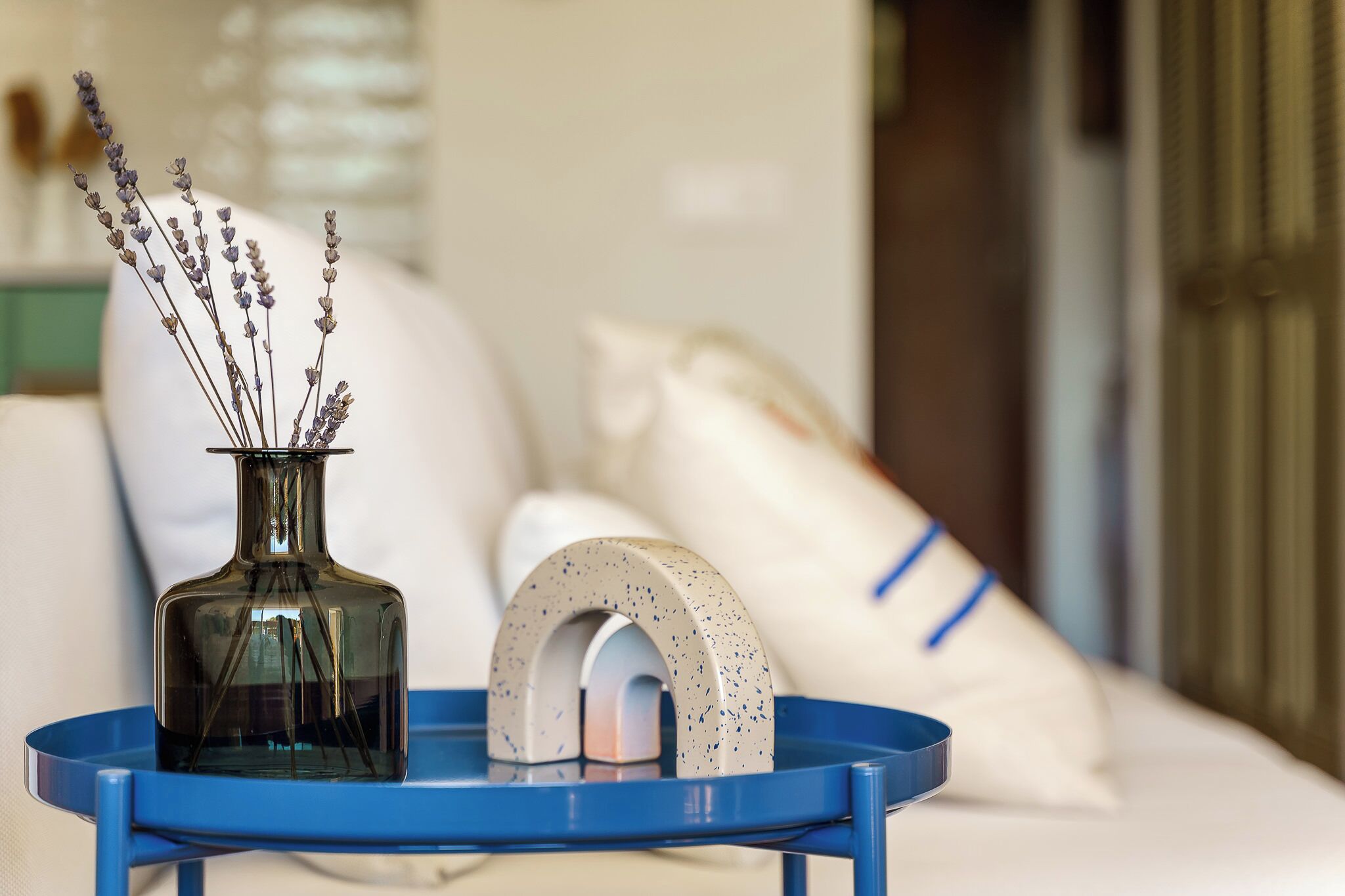 A bed with pillows, a vase with dried flowers, and a blue tray with a decorative object.