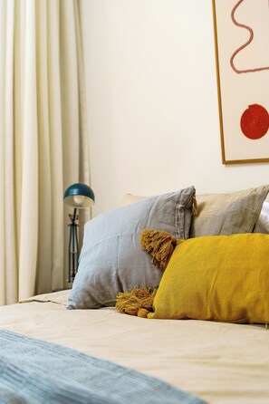 Ein Bett mit Kissen und einer Lampe in einem Zimmer mit Vorhang und Wandbild.