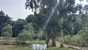 A grassy area with large rocks, a pond, and white plastic chairs arranged around a table.