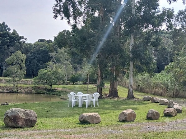 A grassy area with large rocks, a pond, and white plastic chairs arranged around a table.