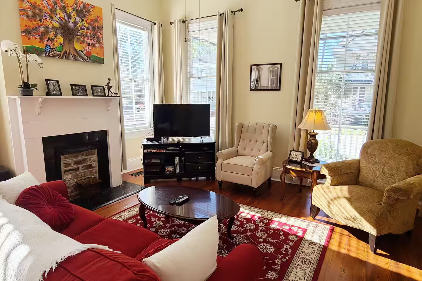 Un salon avec une cheminée, un téléviseur, un canapé rouge, un fauteuil beige et un tapis à motifs.