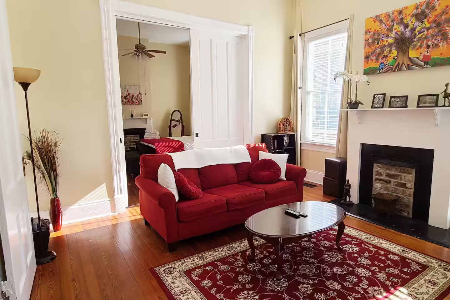 A living room with a red sofa, a coffee table, a fireplace, and a large window.