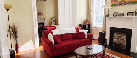 A living room with a red sofa, a coffee table, a fireplace, and a large window.