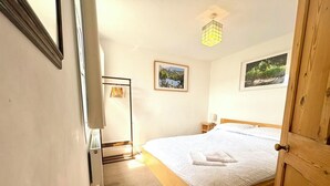 Een slaapkamer met een houten bed, een nachtkastje, een hanglamp en twee ingelijste foto's aan de muur.