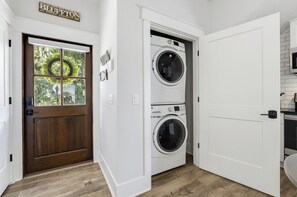 A laundry room with a double-door washing machine and dryer, a wooden door with a window, and a sign above the door. - May River Cottage on Lawrence street, old Town. (Bluffton)