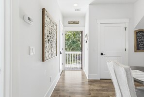 A hallway with a white door, a sign reading 'Blufton,' and a view of a balcony with greenery.