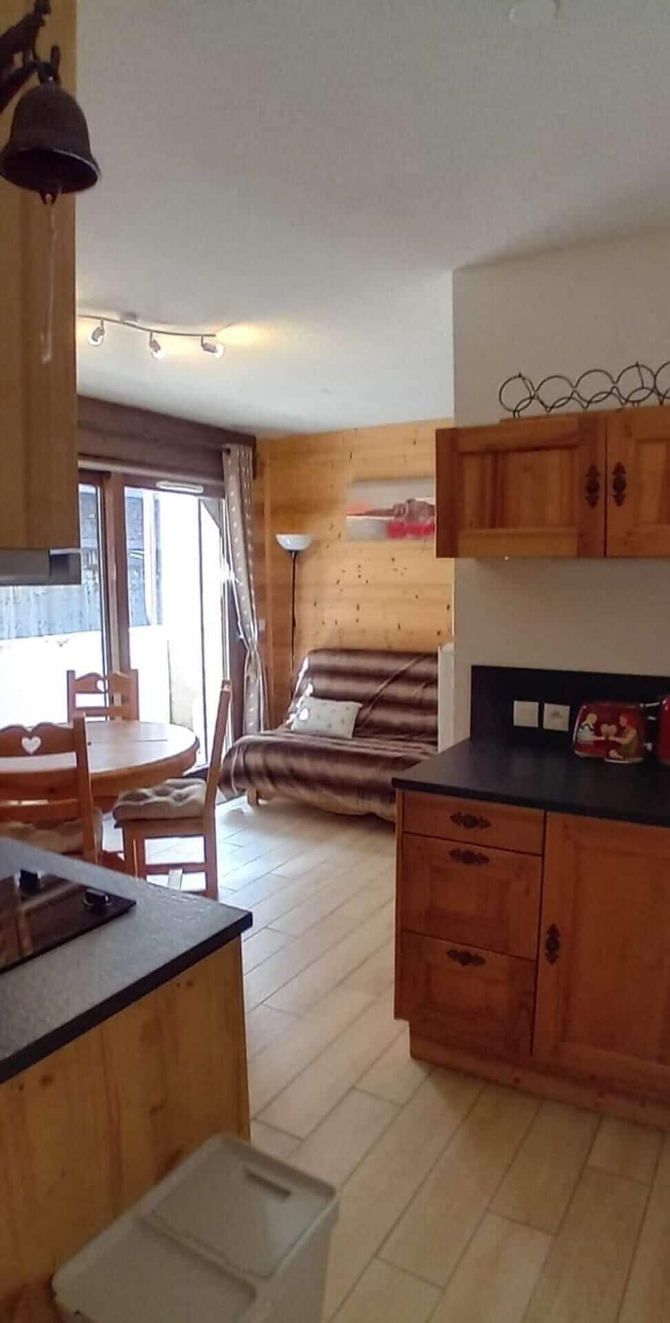 A compact kitchen with wooden cabinets, a dining table with chairs, and a sofa in the living area.
