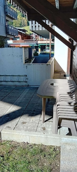 An outdoor seating area with a table and chairs, a concrete floor, and a view of buildings in the background. - 100m from ski slopes, Ground floor, terrace, parking, tv, 34m², Les Gets (Les Gets)