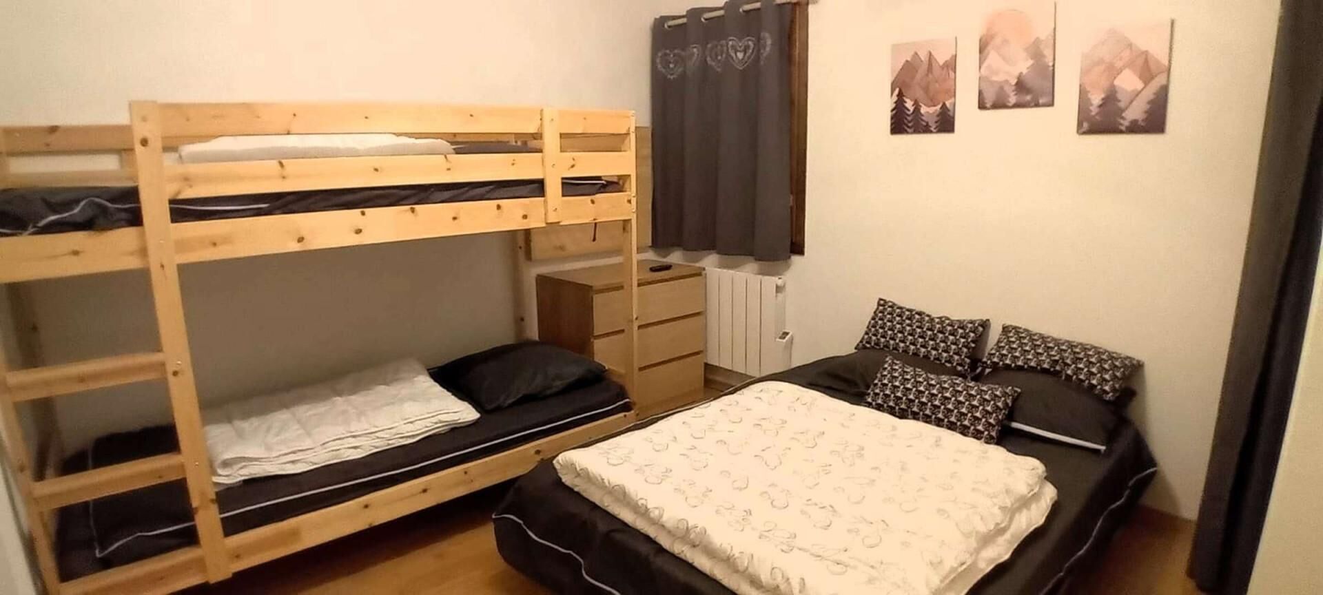 Een kamer met een stapelbed, een enkel bed, een dressoir en een radiator.