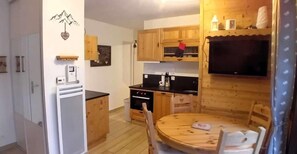 A compact kitchen with wooden cabinets, a dining table, and a television mounted on the wall. - 100m from ski slopes, Ground floor, terrace, parking, tv, 34m², Les Gets (Les Gets)