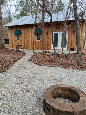 Une cabane en bois avec un chemin de gravier menant à un foyer en pierre.