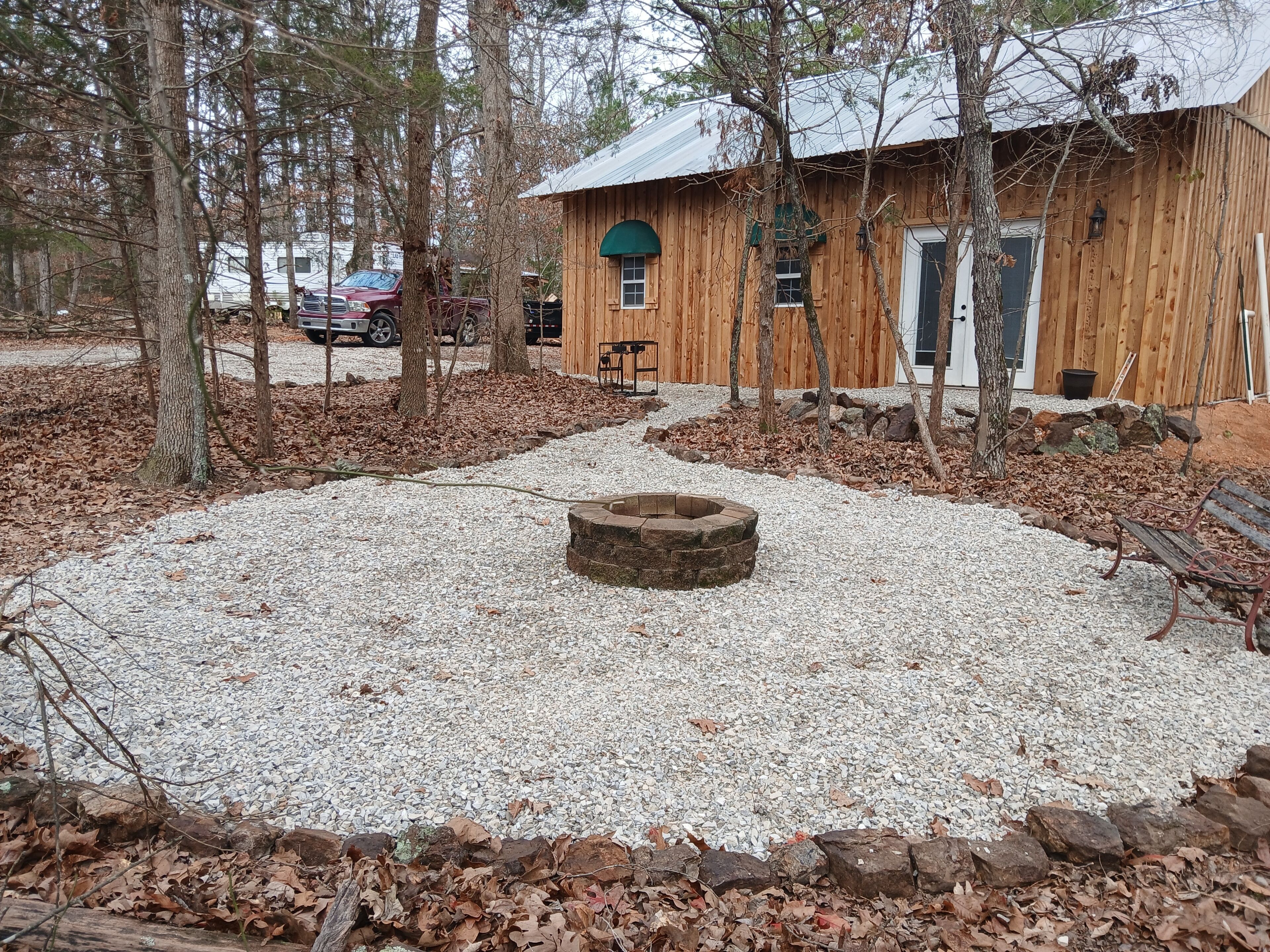 A rustic wooden cabin with a gravel patio, a fire pit, and a bench.