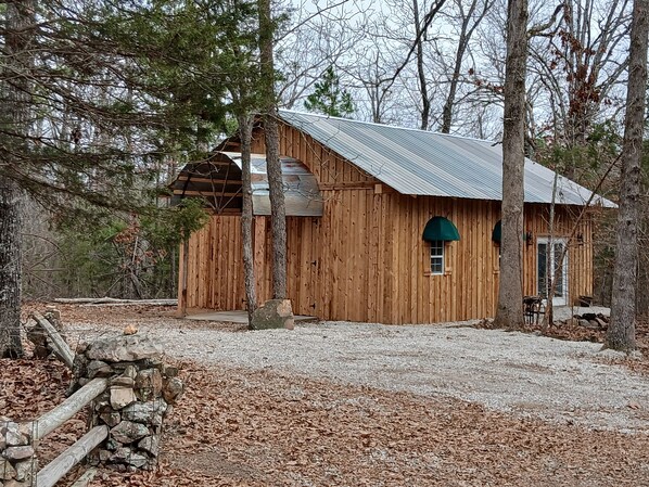 A rustic wooden cabin with a metal roof, surrounded by trees and a gravel driveway.