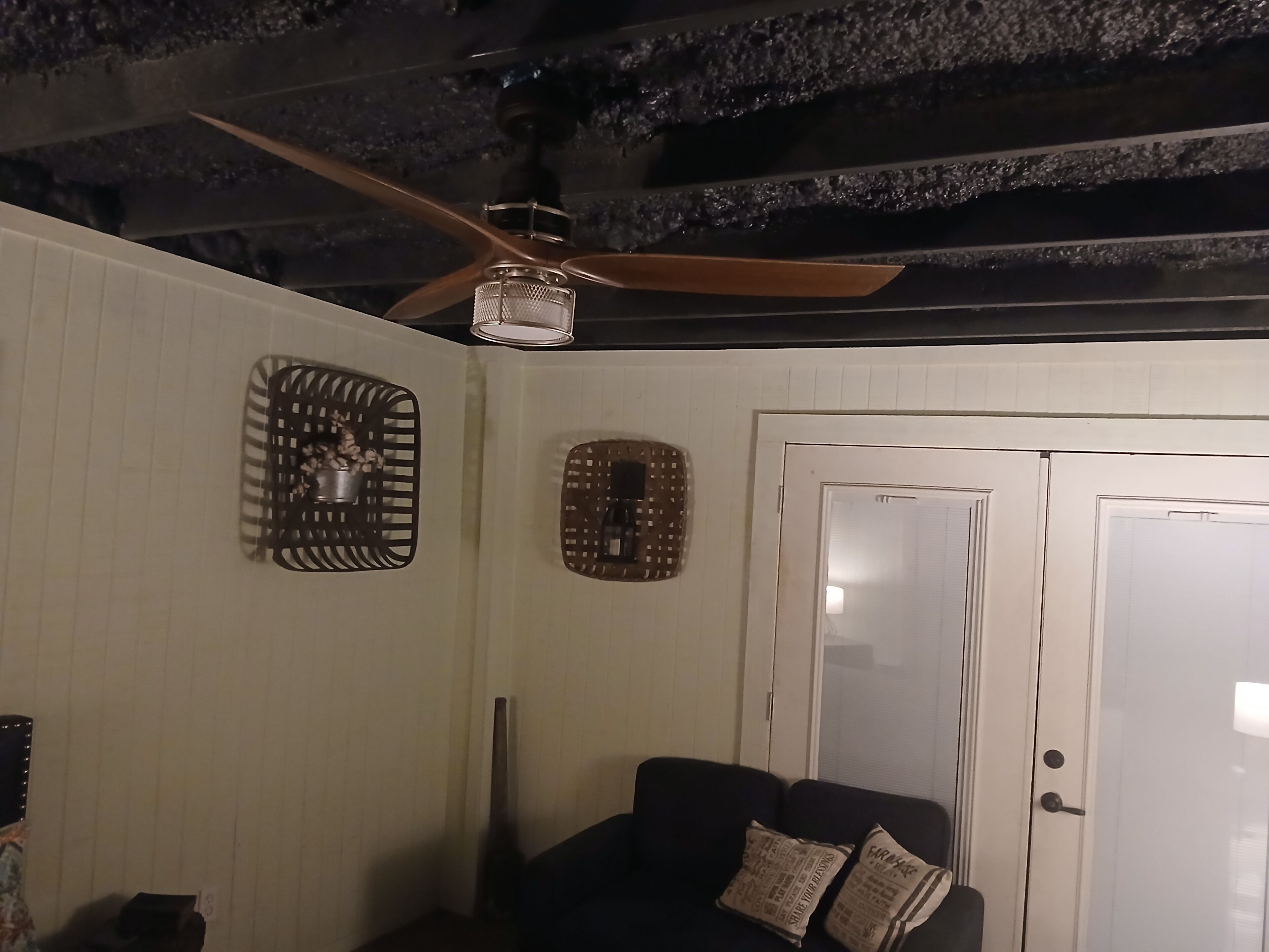 Ein Zimmer mit Deckenventilator, einer Tür und einer Couch mit gemusterten Kissen.