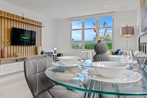 A modern dining area with a glass table, white plates, and a flat-screen TV mounted on a wooden panel. - Caribbean Sea View | Tmobile District Free Parking (SanJuan)