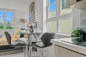A modern kitchen with a glass-top dining table, stainless steel chairs, and a view of the city. - Caribbean Sea View | Tmobile District Free Parking (SanJuan)